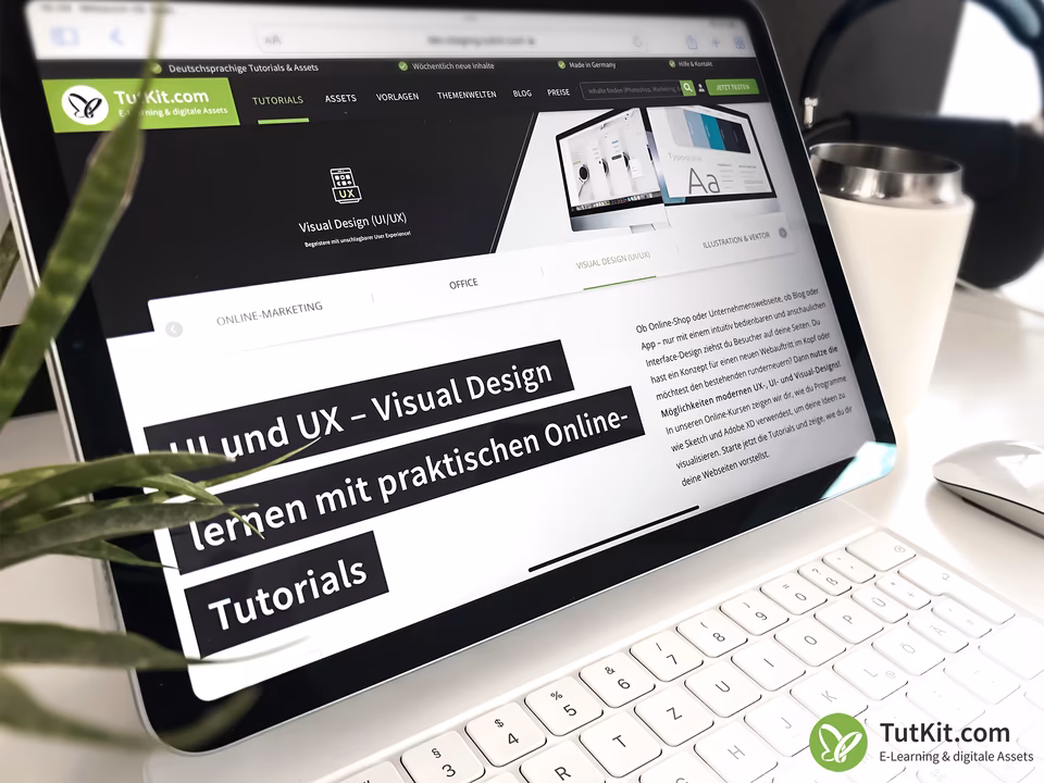 Tablet mit ge&ouml;ffneter TutKit.com-Seite &bdquo;UI und UX &ndash; Visual Design lernen mit praktischen Online-Tutorials&ldquo; auf einem Schreibtisch mit Pflanze und Kaffeebecher